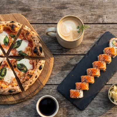 Restaurant wall decor, a sliced pizza, a latte and sushi rolls on a rustic wooden table in warm evening light
