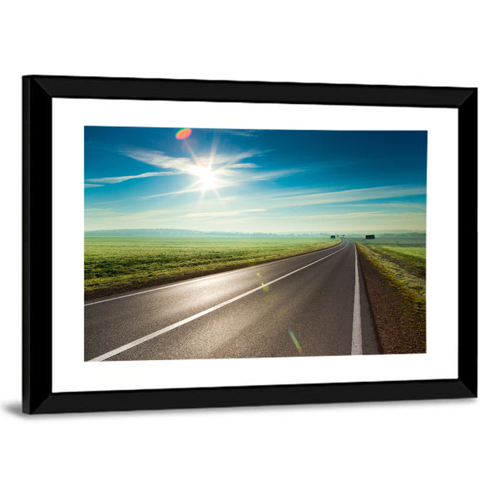 Sunlit Road Through Green Field Wall Art as a framed print
