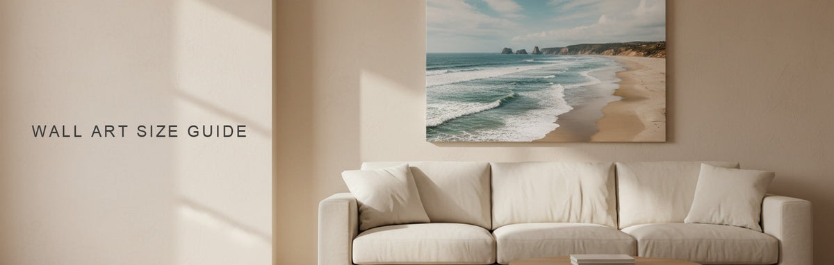 Wall art size guide in a living room with a seven foot sofa: a wide coastal landscape canvas two thirds the width of the sofa