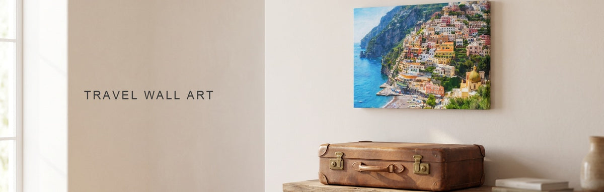Travel wall art in a living room: a canvas of the Positano coast above a console with a vintage leather suitcase