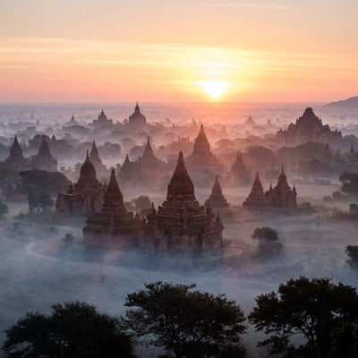 Buddhism wall art, brick stupas and temples rising from low morning mist on a plain under a gold and rose sunrise sky