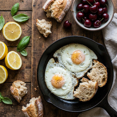 Kitchen wall decor, overhead close-up of fried eggs in a cast iron pan with bread, lemons, basil and cherries